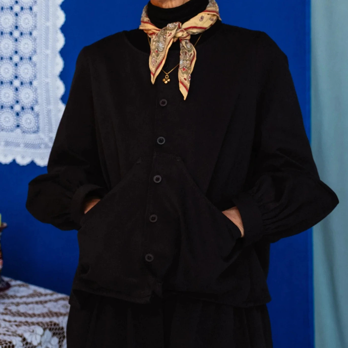 Person wearing a black outfit with a patterned scarf against a blue background