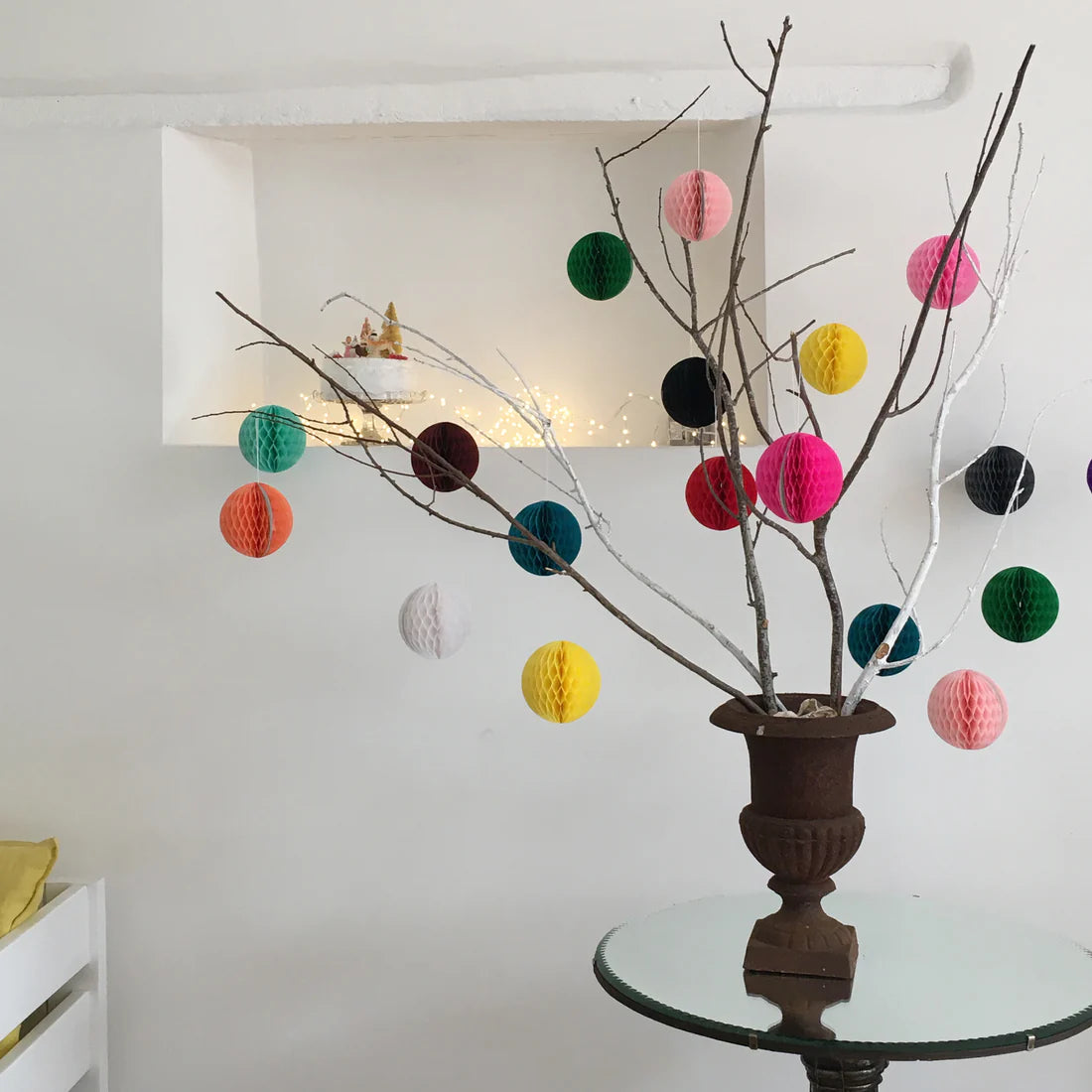 Decorative branches with colorful paper balls in a vase on a glass table.
