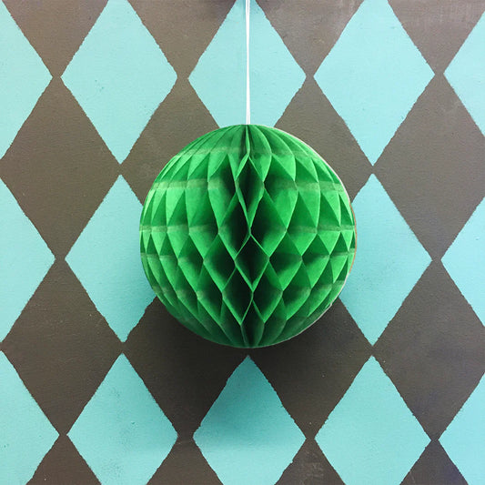 Green paper honeycomb ball hanging against a diamond-patterned background
