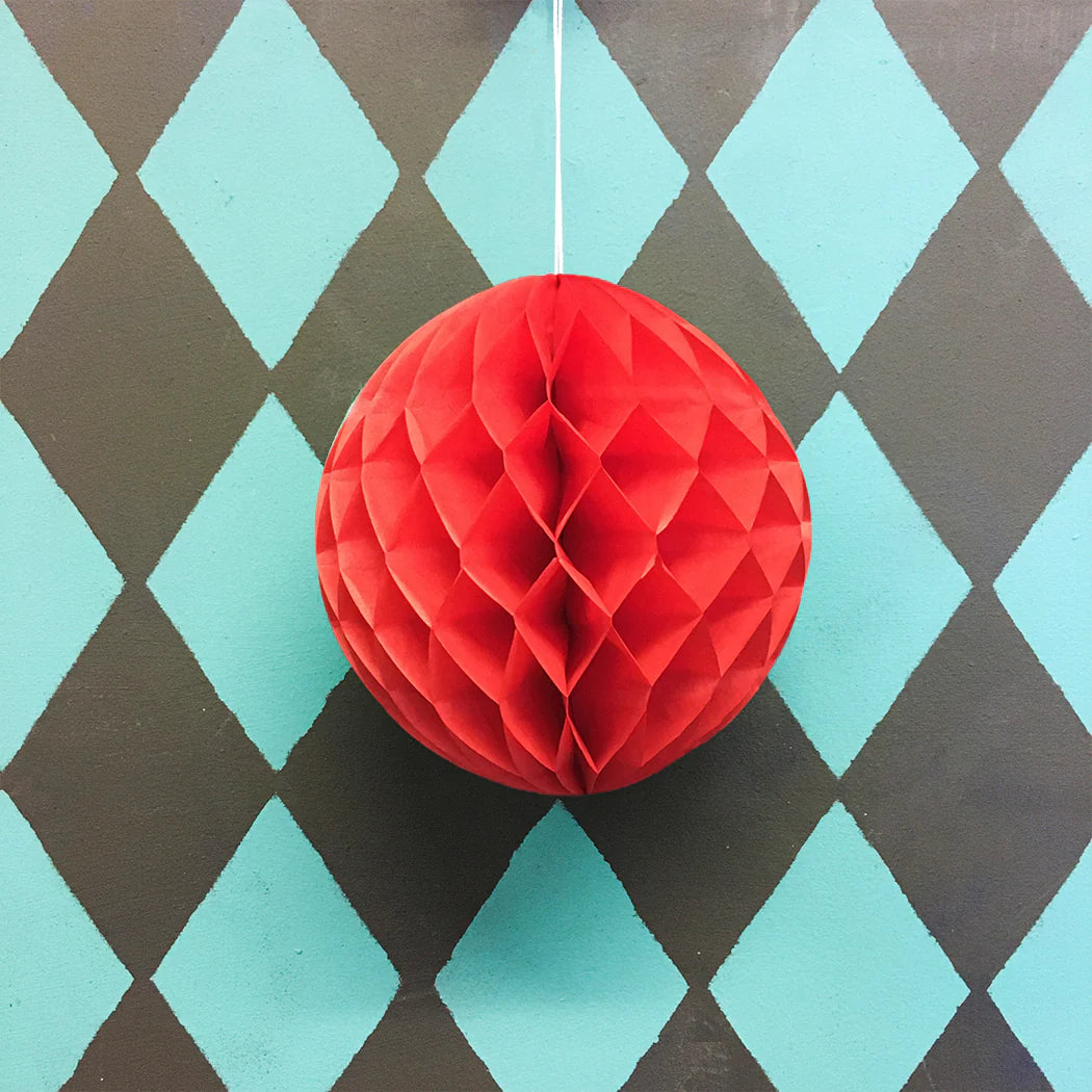 Red paper honeycomb ball hanging against a diamond-patterned background