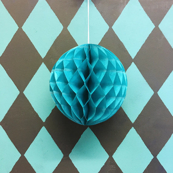 Teal paper honeycomb ball hanging against a diamond-patterned background