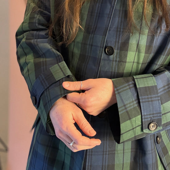Person wearing a green and blue plaid shirt with buttons, holding a phone.