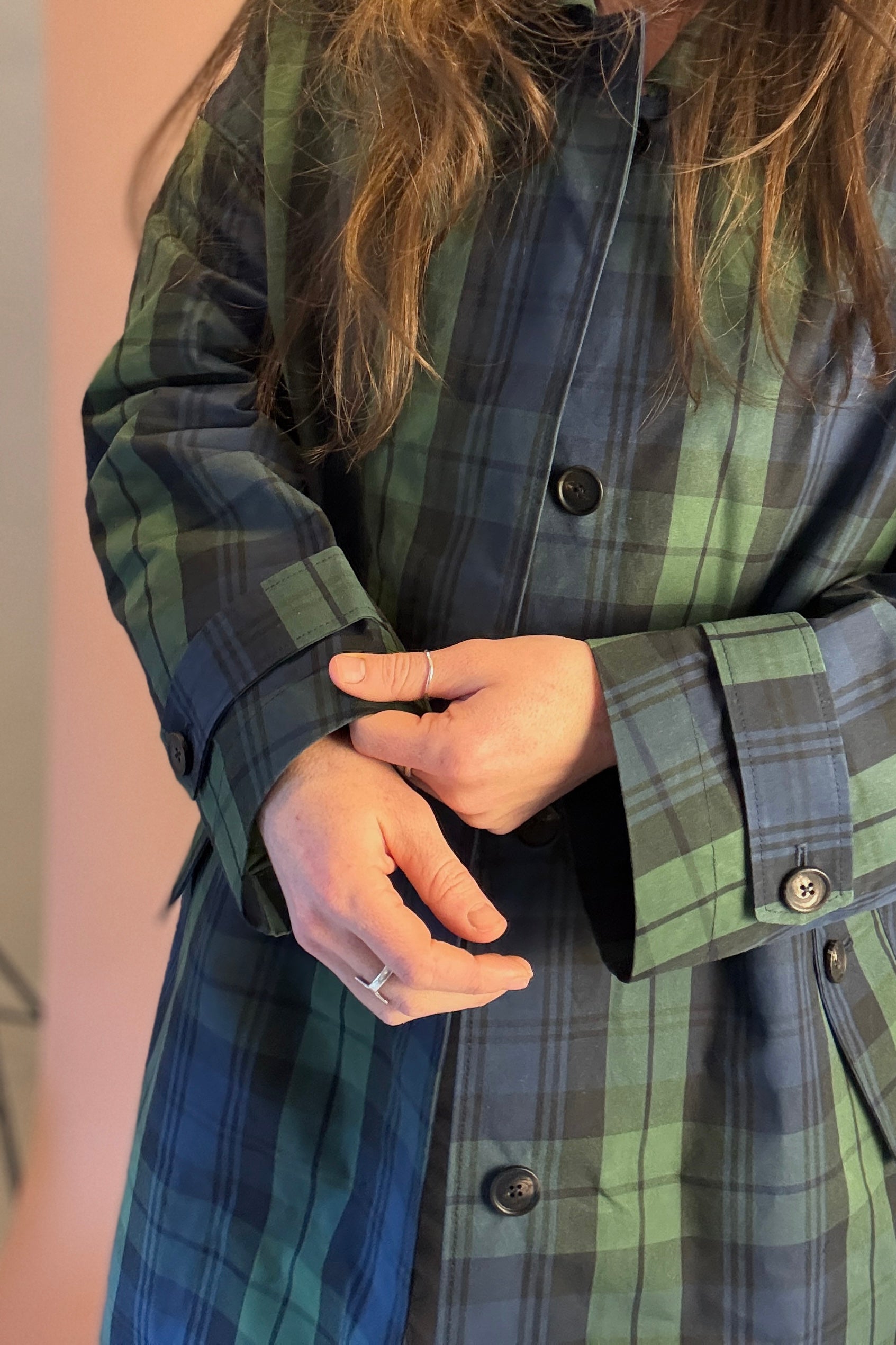 Person wearing a green and blue plaid shirt with buttons, holding a phone.