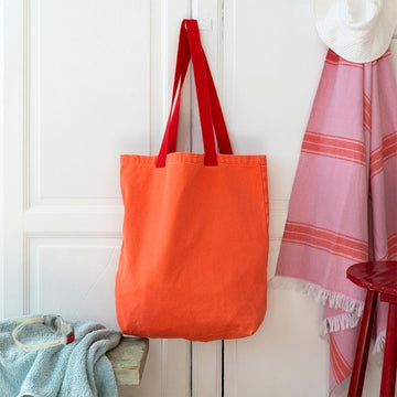 Coral tote bag with contrasting red handles hanging against a white wardrobe with a towel and blanket in the background