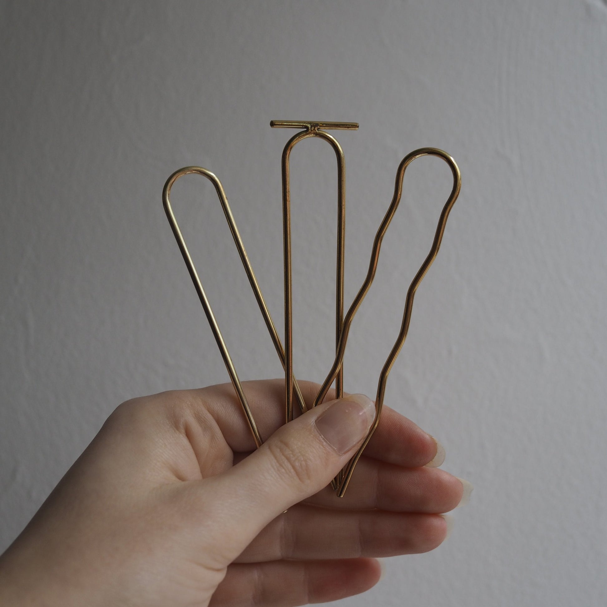 Hand holding three gold hair clips against a plain background