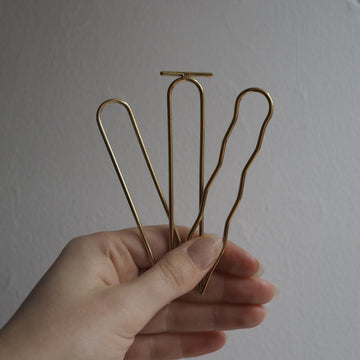 Hand holding three gold hair clips against a plain background