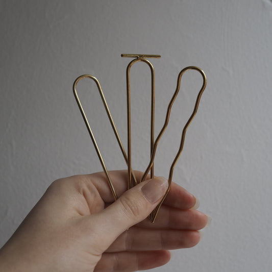 Hand holding three gold hair clips against a plain background
