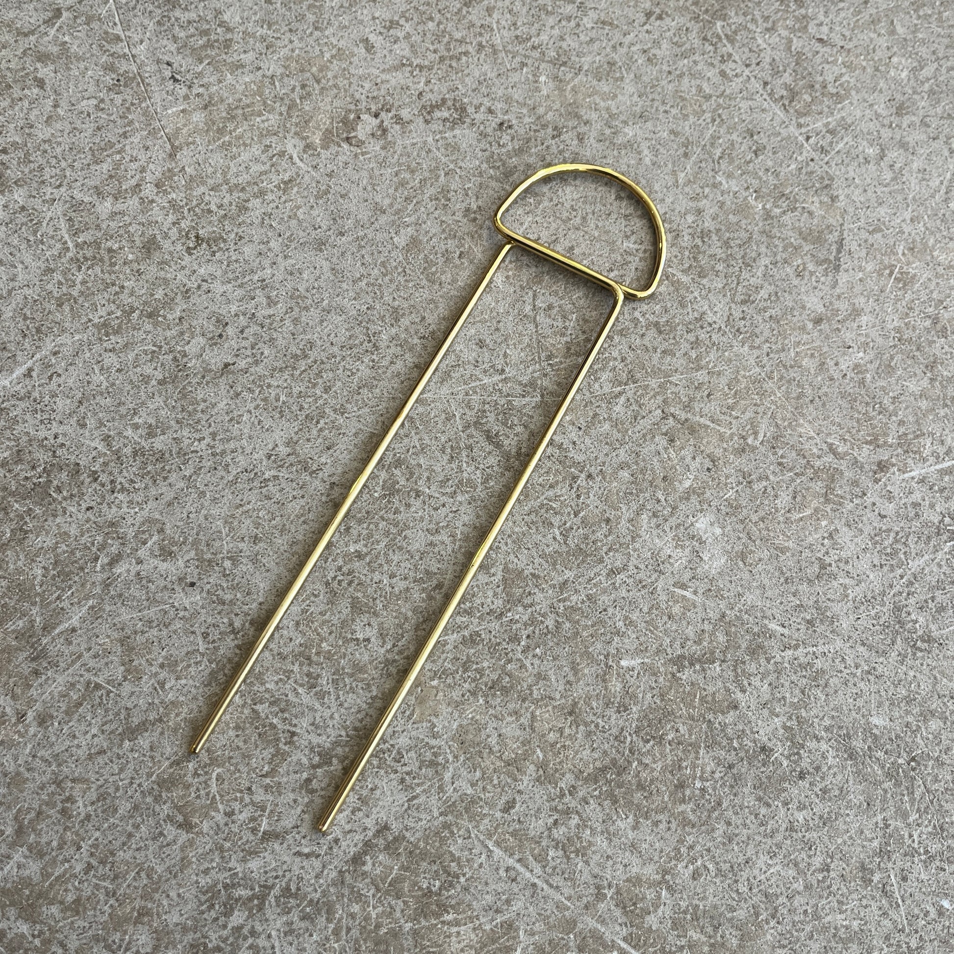 a semi circle brass hairpin on a concrete background