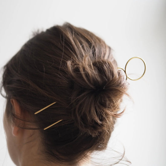 Close-up of a person's hair with gold hairpins against a white background