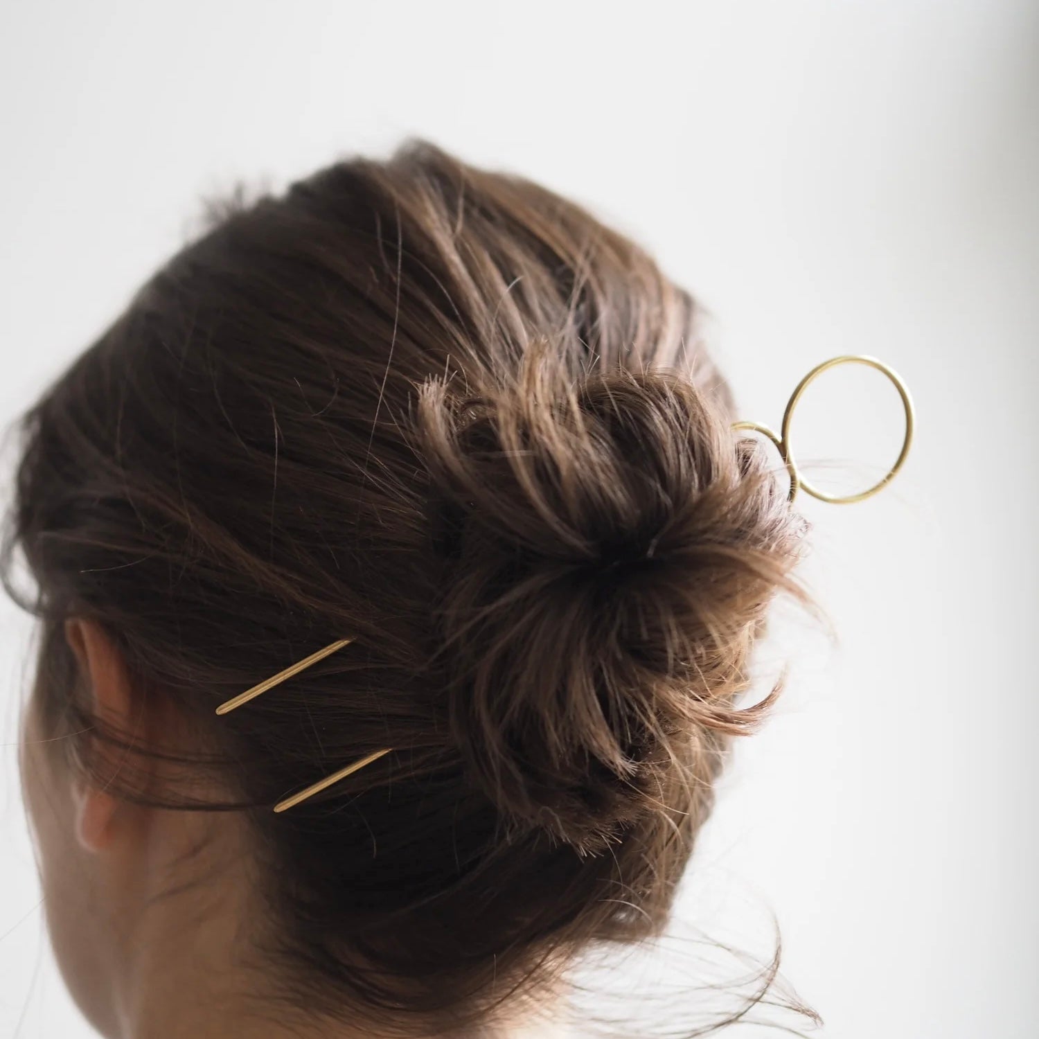 Close-up of a person's hair with gold hairpins against a white background