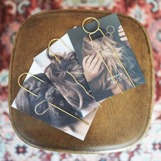Gold hair pins on display cards on a wooden stool with a patterned rug background