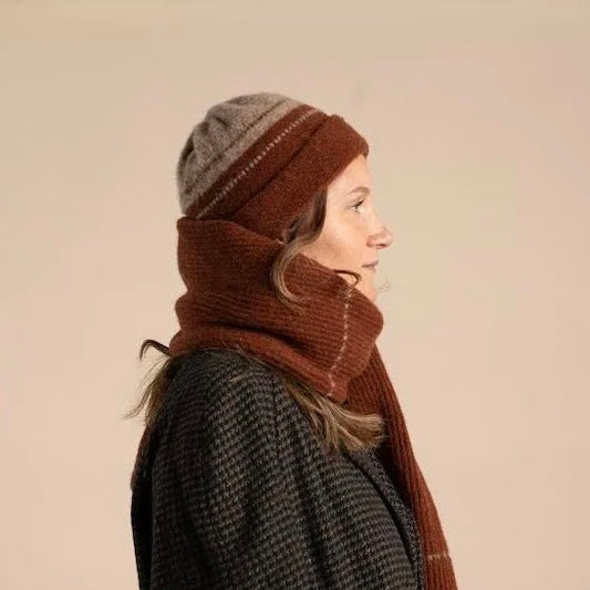 Person wearing a brown knitted hat and scarf on a beige background