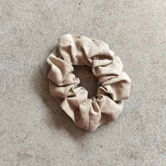 A taupe colored bio linen scrunchie on a textured background.