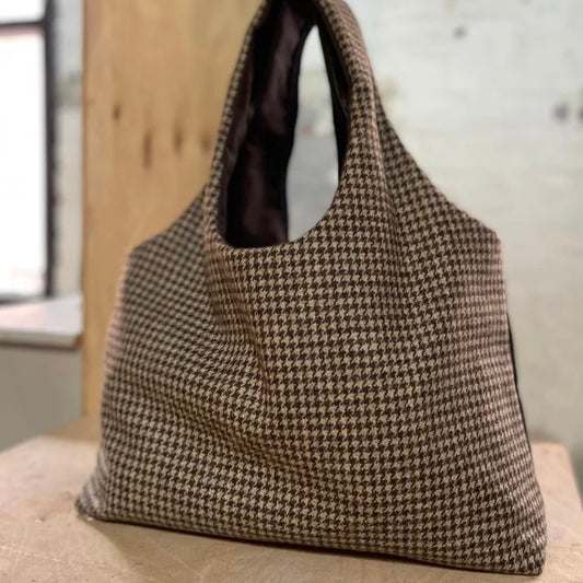 Houndstooth tweed patterned large tote bag on a textured wooden surface with a neutral background