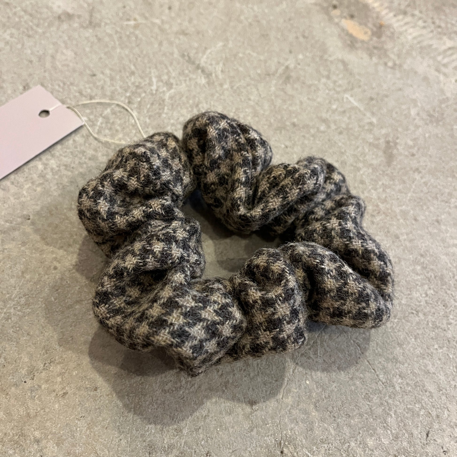 Textured tweed scrunchie on a concrete surface with a label