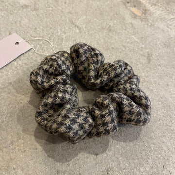 Textured tweed scrunchie on a concrete surface with a label