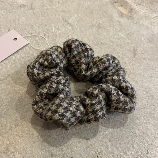 Textured tweed scrunchie on a concrete surface with a label