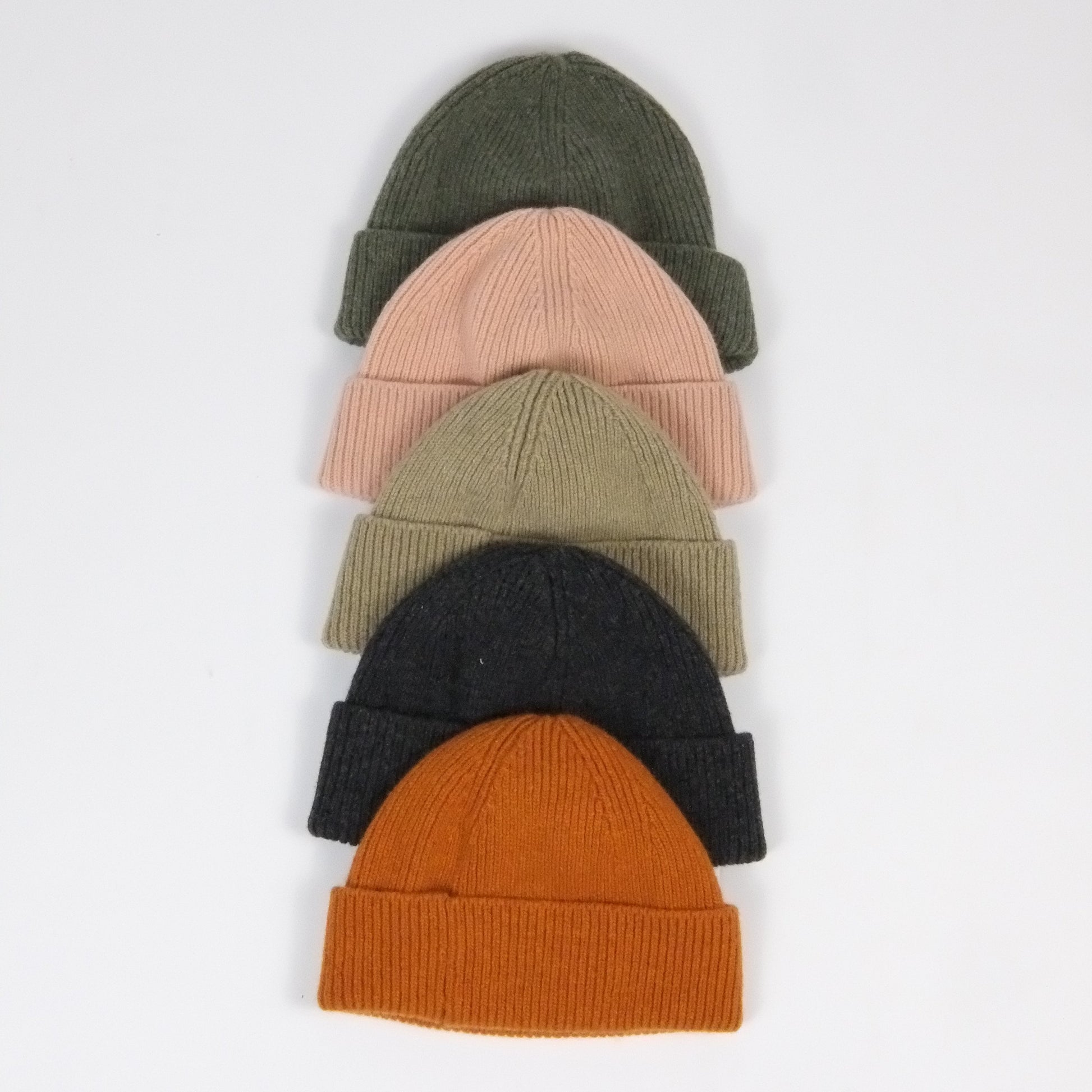 Five knit beanies in different colors arranged on a light gray background