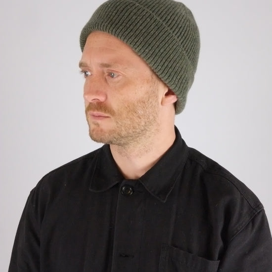 Man wearing a black jacket with a logo and a green beanie on a white background