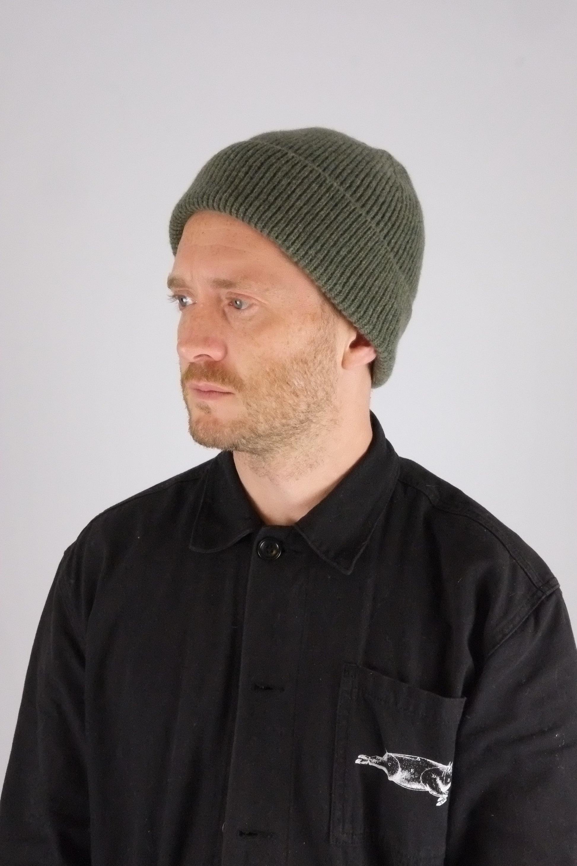 Man wearing a black jacket with a logo and a green beanie on a white background