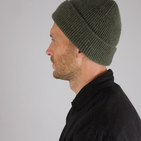 Person wearing a green knit beanie against a plain background