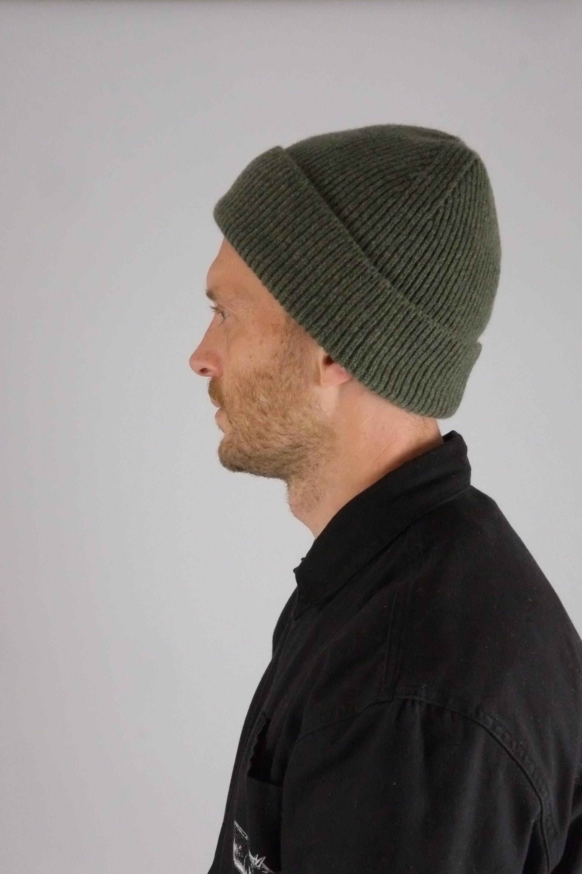 Person wearing a green knit beanie against a plain background