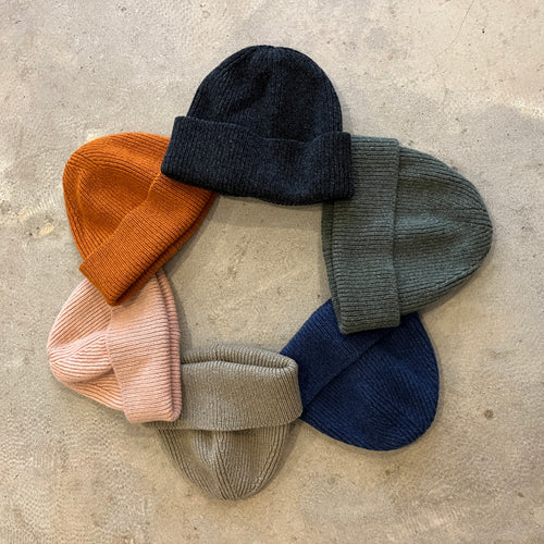 Set of six knit beanie hats in various colors on a concrete surface