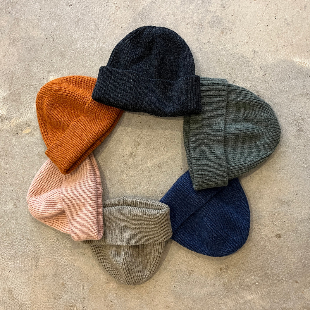 Set of six knit beanie hats in various colors on a concrete surface