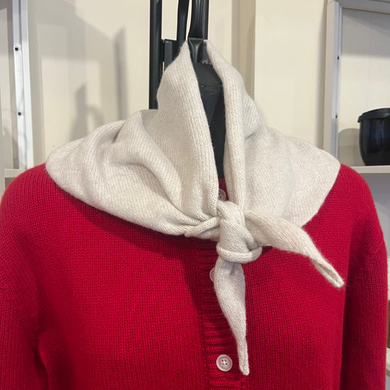 Mannequin wearing a red sweater with a beige scarf draped over it, against a neutral background.