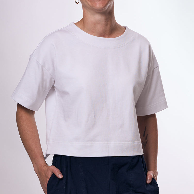 Person wearing a white t-shirt and dark pants on a plain background