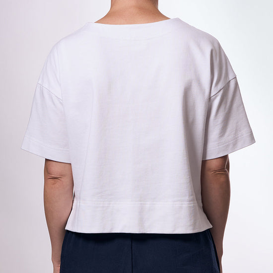 Person wearing a white t-shirt and dark pants on a plain background