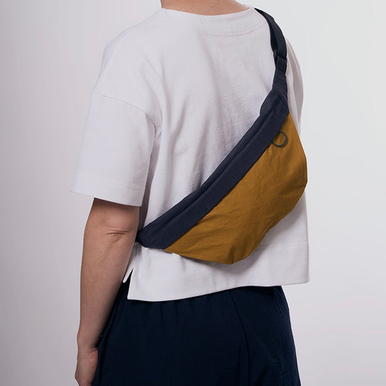 Person wearing a white shirt with a yellow and navy crossbody bag on a plain background
