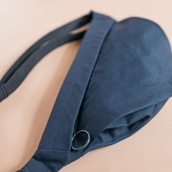 Navy blue bag worn over one shoulder on a beige background