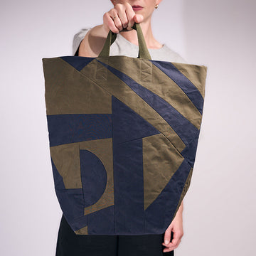 Person holding a large tote bag with geometric design against a plain background