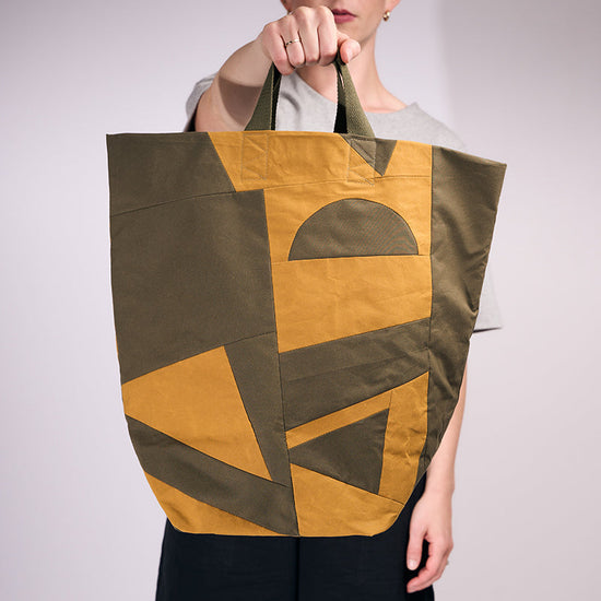 Person holding a large tote bag with geometric design on a plain background