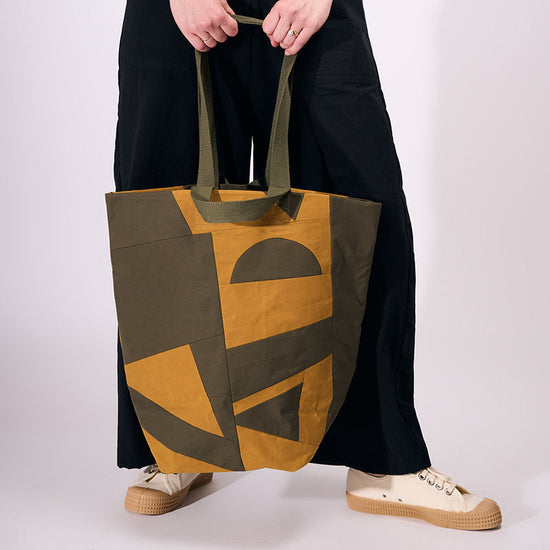Person holding a tote bag with geometric design on a plain background