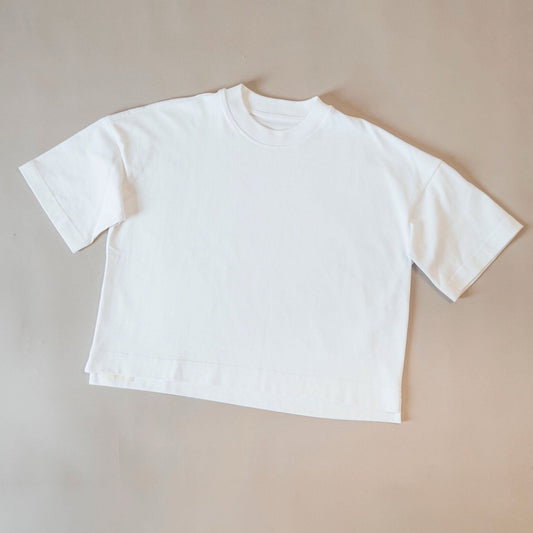 A plain white short-sleeve cropped T-shirt laid flat on a warm beige background.