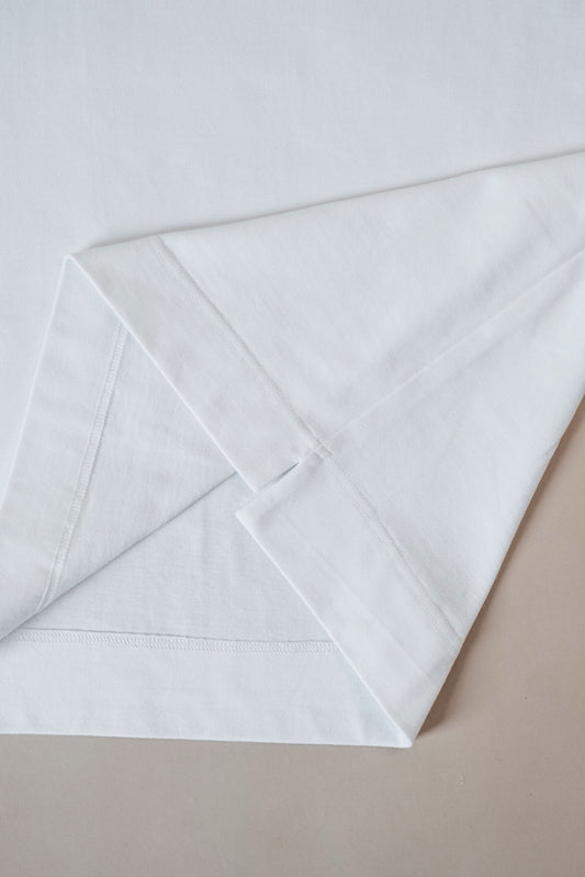 A folded white cotton tshirt with a subtle woven texture, laid flat on a neutral beige surface.
