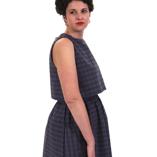 Woman wearing a sleeveless blue and purple check top and skirt on a white background