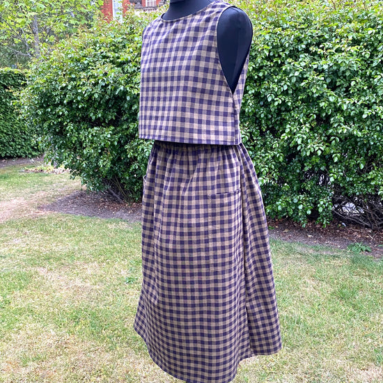 Mannequin wearing a checkered green and black  skirt and top in an outdoor setting with greenery.