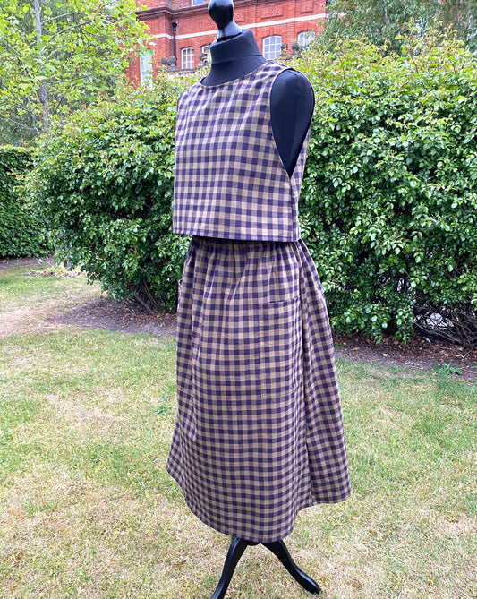 Mannequin wearing a checkered green and black  skirt and top in an outdoor setting with greenery.