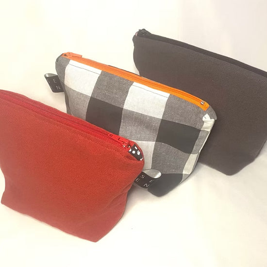 Three pouches in red, black and white checkered, and black with orange zipper on a white background 