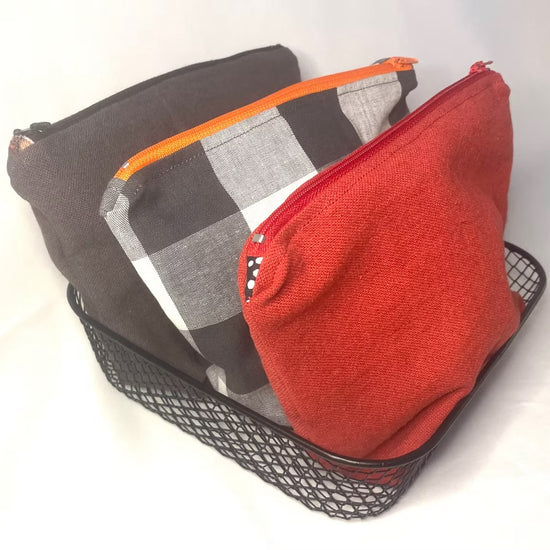 Three toiletry bag pouches in red, grey and check in a black metal tray on a white background