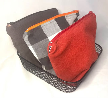 Three toiletry bag pouches in red, grey and check in a black metal tray on a white background