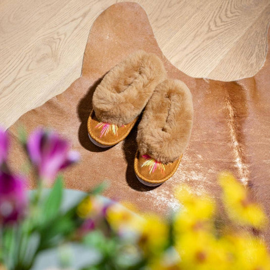 Brown slippers on a wooden floor with flowers in the foreground