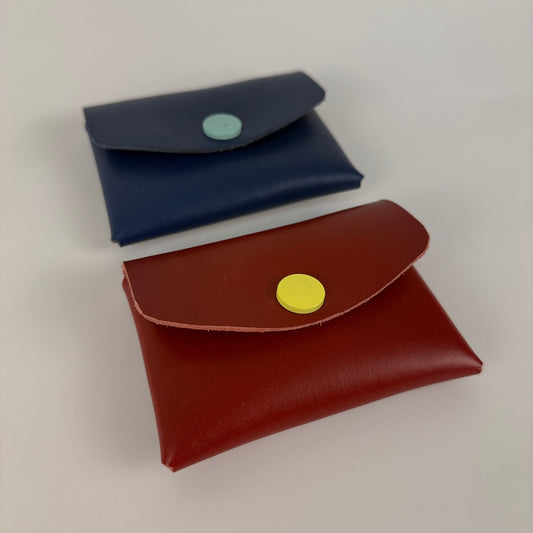 Two leather pouches, one blue and one red, with button closures on a light gray background.