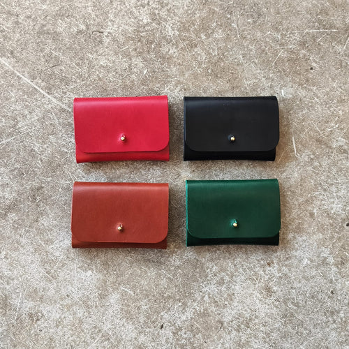 Four small leather wallets in red, black, and green on a textured surface