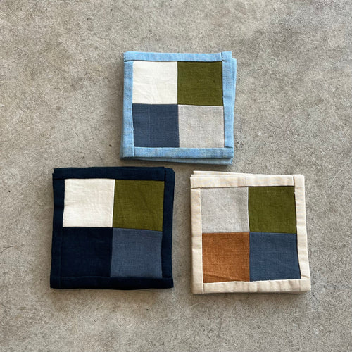 Three square fabric coasters with patchwork patterns on a concrete surface