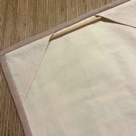 Cream linen back with stone coloured trim of a quilted wall hanging with a wooden rod for hanging