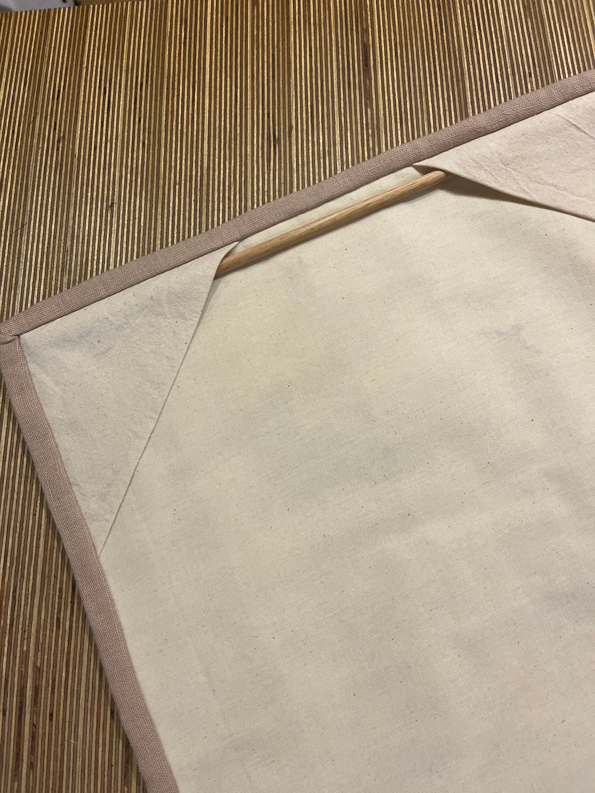 Cream linen back with stone coloured trim of a quilted wall hanging with a wooden rod for hanging